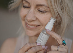 A woman smiling and holding a bottle of Bare Nature Renew Hyaluronic Acid Gel Serum close to her face.